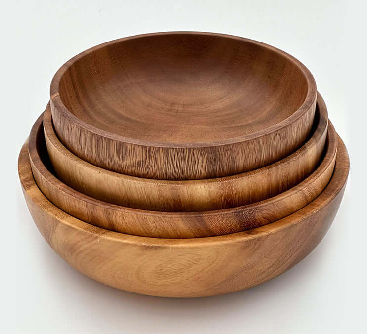Hand carved acacia bowls stacked together, showcasing the unique wood grain and rich tones of each handcrafted bowl.